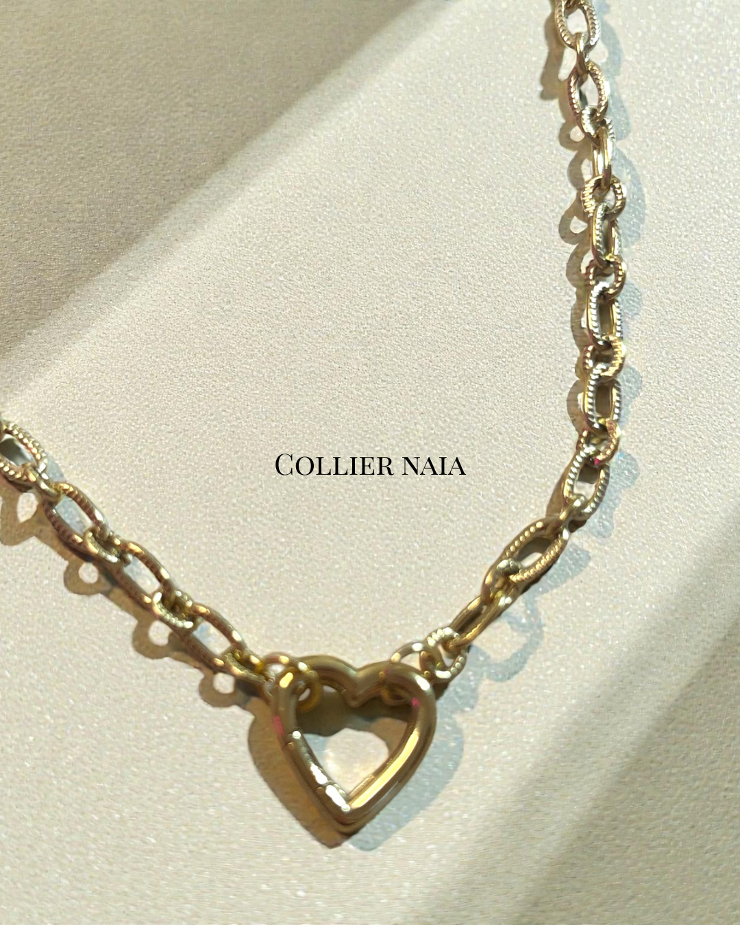 Collier Naia en acier inoxydable doré, chaîne texturée avec pendentif cœur ajouré, longueur 42 cm, photographié en lumière naturelle sur fond crème.