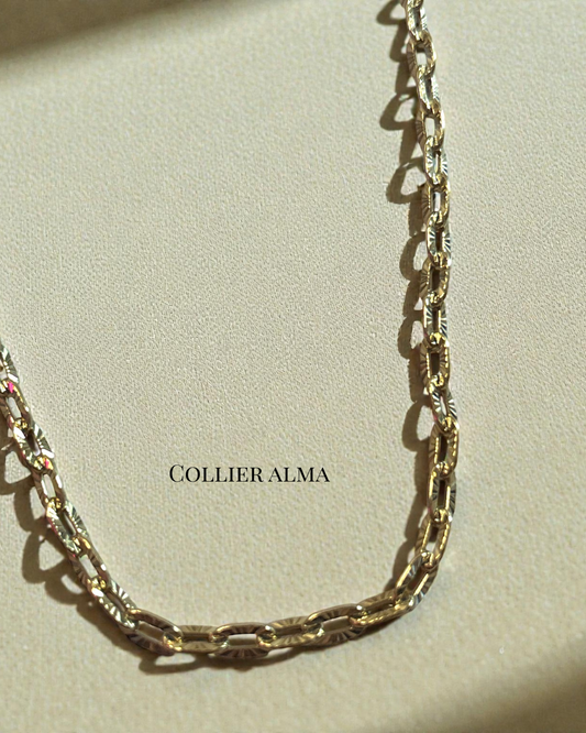 Collier Alma en acier inoxydable doré, chaîne à maillons texturés, posé sur fond beige lumineux.