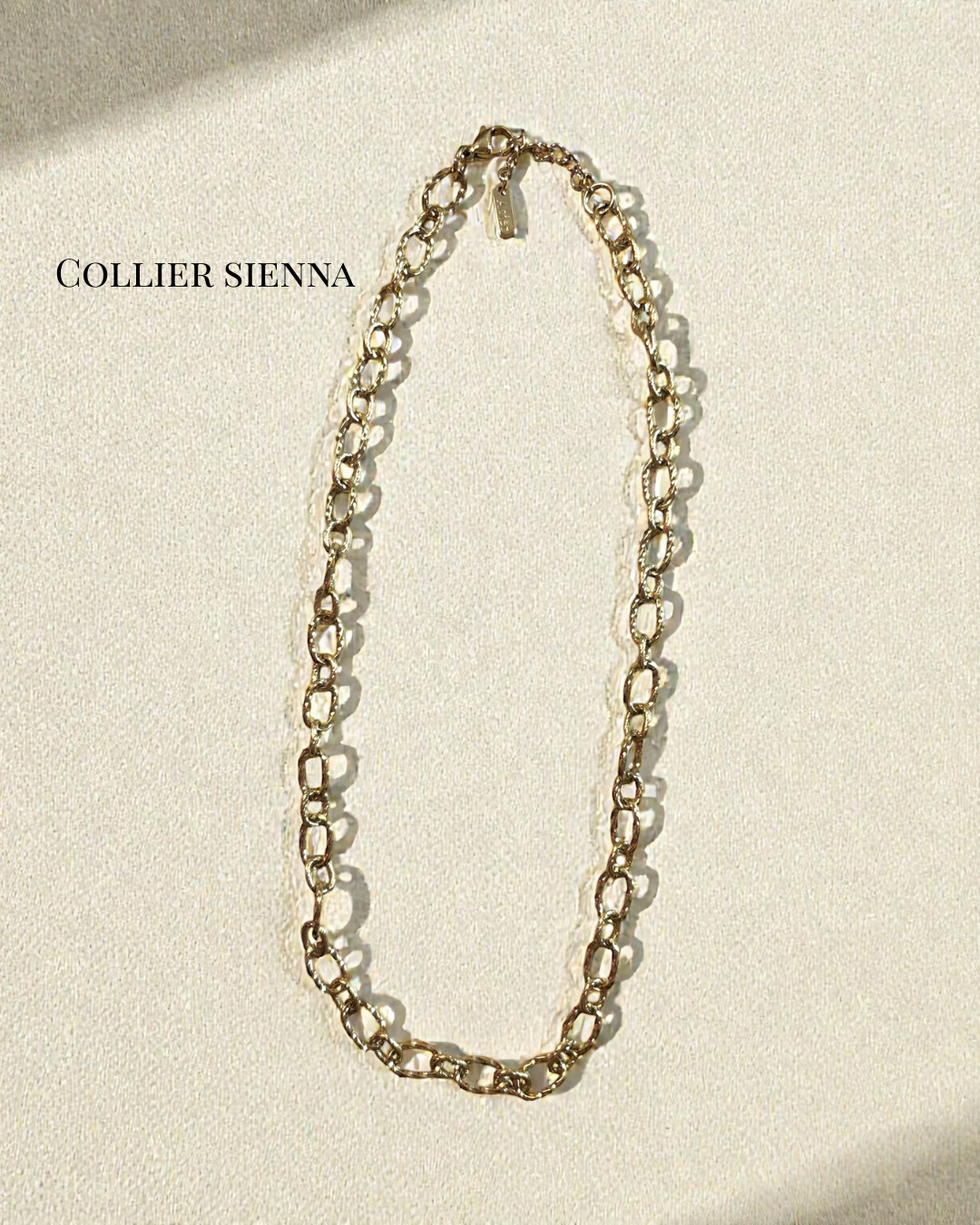 Collier Sienna en acier inoxydable doré, maillons martelés, longueur 42 cm avec chaînette 3 cm, photographié sur fond crème.