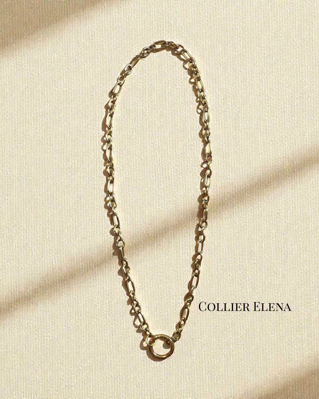 Collier Elena en acier inoxydable doré, chaîne texturée avec grand anneau central, longueur 42 cm, photographié sur fond crème en lumière naturelle.