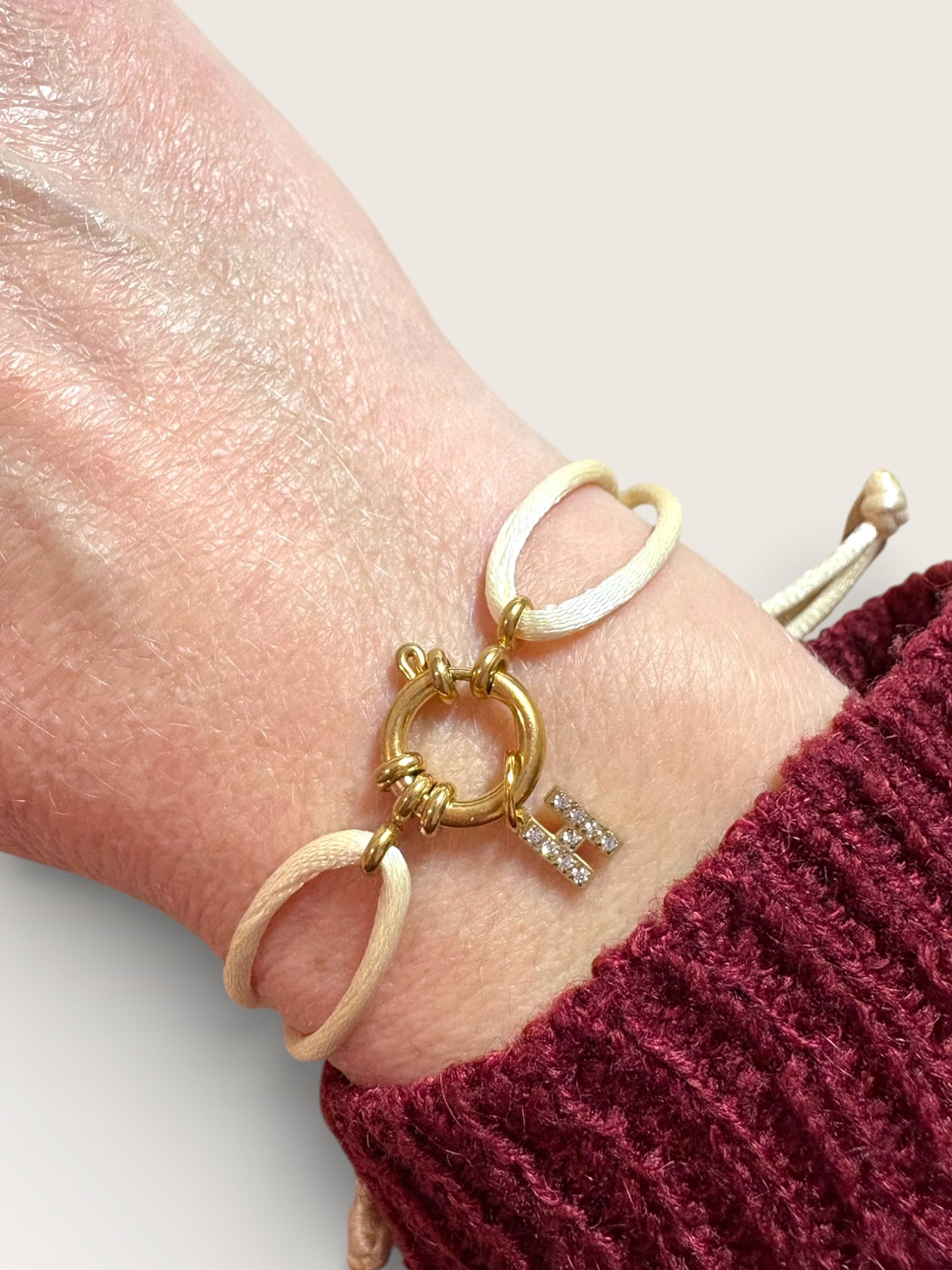 Bracelet cordon beige avec anneau et initiale dorée sertie de strass porté au poignet – Collection Pour Toi By Maryon