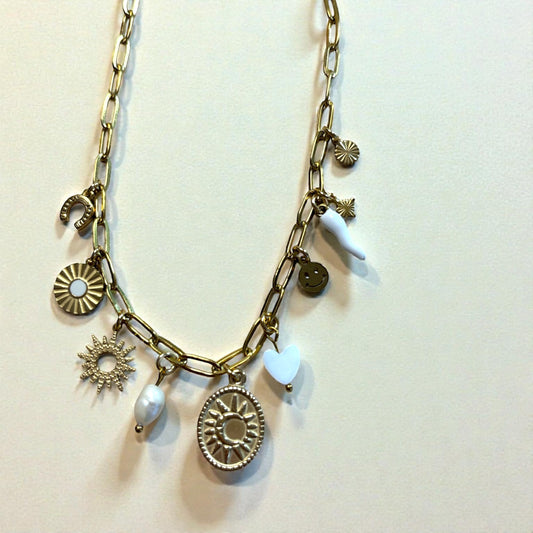 Collier doré en acier inoxydable avec chaîne à maillons rectangulaires, composé de plusieurs charms symboliques : soleil central texturé, petit soleil, cœur blanc, fer à cheval, smiley doré, corne porte-bonheur blanche et perle d’eau douce. Bijou talisman lumineux au style good vibes.